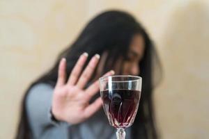 rinunciare all'alcool una giovane donna al tavolo rifiuta con la mano un bicchiere di vino rosso fuoco selettivo foto