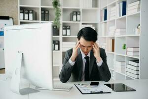 asiatico uomo d'affari è stressato, annoiato, e troppi pensieri a partire dal Lavorando su un' tavoletta a il ufficio. foto