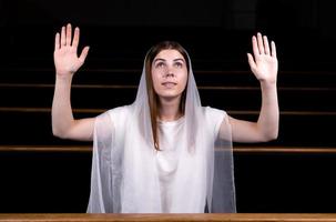 una giovane ragazza modesta con un fazzoletto in testa è seduta in chiesa e prega foto