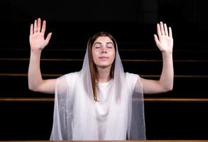 una giovane ragazza modesta con un fazzoletto in testa è seduta in chiesa e prega foto