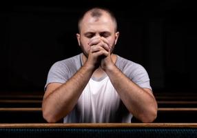 un uomo cristiano in camicia bianca è seduto e prega con cuore umile nella chiesa