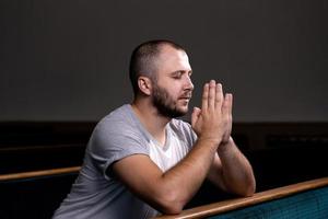 un uomo cristiano in camicia bianca è seduto e prega con cuore umile nella chiesa