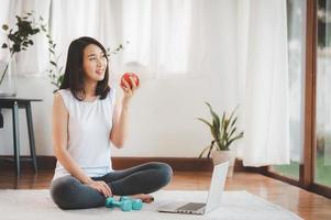donna che mangia mela prima di fare lezione di ginnastica in linea dal computer portatile foto
