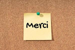 merci - parola di ringraziamento in lingua francese sulla nota gialla sulla bacheca di sughero foto
