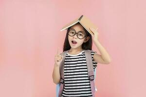 scolara abbracciare libro indossare zaino sorridente isolato su rosa sfondo foto