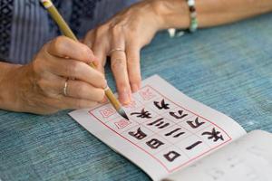 chiudere le mani della donna senior pratiche di scrittura calligrafia di caratteri cinesi tradizionali foto