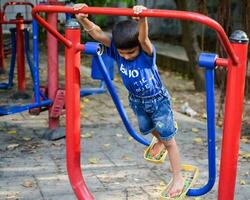 asiatico ragazzo fare routine esercizio nel società parco durante il mattina volta. carino poco ragazzo esercizio e Palestra per mantenere lui stesso in forma per vita. del bambino esercizio all'aperto sparare foto