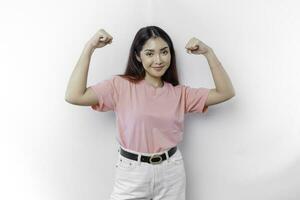 eccitato asiatico donna indossare un' rosa maglietta mostrando forte gesto di sollevamento sua braccia e muscoli sorridente con orgoglio foto