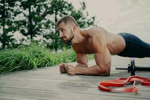 in forma barbuto uomo fa tavola esercizio all'aperto, Spettacoli resistenza e motivazione, pose vicino gli sport attrezzatura. foto