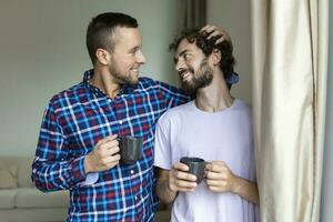 giovane gay coppia nel amore guardare su il finestra. Due giovane androgino uomini sorridente insieme e avendo caffè. foto