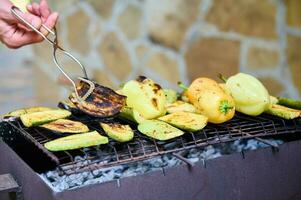 avvicinamento maschio mano retromarcia fetta di zucchine mentre grigliate verdure al di sopra di fiammeggiante carbone foto