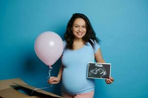 incinta donna aspettandosi un' bambino ragazza, sorrisi allegramente, in posa con rosa Palloncino e ultrasuono Immagine, isolato su rosa foto