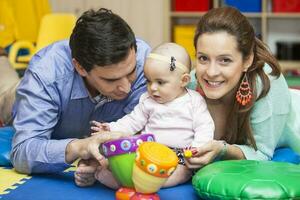 giovane genitori giocando con loro sei mesi vecchio bambino ragazza al chiuso. con mamma e papà apprendimento per giocare il batteria foto