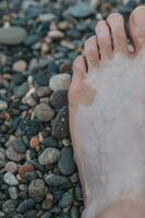 maschio spoglio piede durante spiaggia vacanza su caldo bagnato ciottoli di il oceano foto