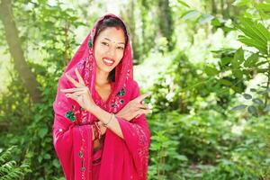 giovane bellissimo nepalese donna indossare saree in piedi nel un' naturale sfondo di foresta Tenere sua mani di sua viso foto