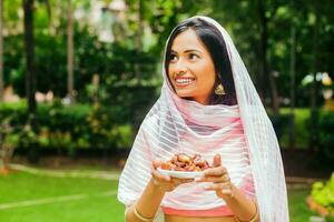 giovane bellissimo indiano donna Tenere un' piatto pieno di date nel un' parco foto