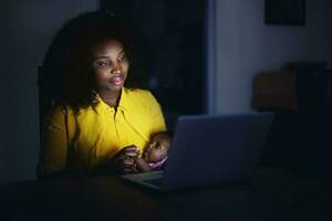 madre seduta a notte con il bambino nel davanti di il il computer portatile foto