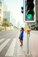 bellissimo africano donna attraversamento il strada su un' strada di dubai foto