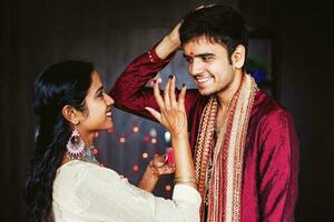 indiano donna è dando benedizioni per il uomo di mettendo tika su il suo fronte mentre indossare tradizionale etnico Abiti foto