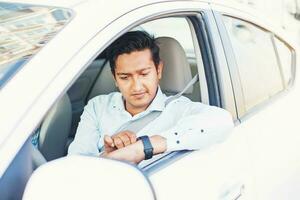 giovane indiano uomo guardare a inteligente orologio mentre seduta nel un' auto foto