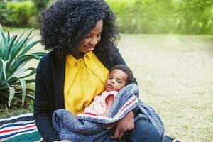 africano donna Tenere sua bambino avvolto nel coperta nel il parco foto