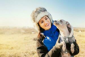 un' giovane felicemente sorridente caucasico donna indossare inverno Abiti giocando con sua cane all'aperto foto