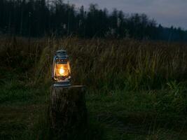 un vecchio olio lanterna con un' illuminato fuoco sta su il ceppo all'aperto a notte. morbido caldo giallo leggero di un vecchio cherosene lampada. foto