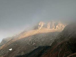 atmosferico spettrale paesaggio con sfocato sagome di acuto rocce nel Basso nuvole. drammatico Visualizza per grande montagne sfocato nel pioggia foschia nel grigio Basso nuvole. diagonale pendenza di il montagna foto