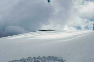 grande nevoso cupola su montagna superiore, il inverno superiore di un' montagna sotto un' drammatico cielo. atmosferico minimalista alpino paesaggio. meraviglioso montanaro scenario. foto