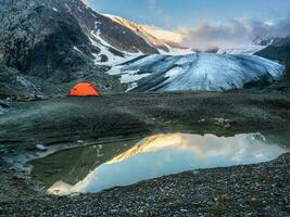 arancia rinforzata tenda contro il sfondo di un' ghiacciaio su un' alta altitudine altopiano. alpinismo campo a il blu lago con riflessione. aktru. foto