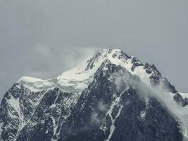 atmosferico alpino paesaggio con innevato montagna superiore sotto neve grigio cielo. eccezionale scenario con bellissimo a punta picco con neve e alto nevoso montagna parete con Basso nuvole. foto