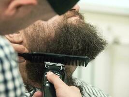 Rifinitura barba con clippers nel un' barbiere negozio. vicino su. foto