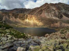 luminosa raggio di luce del sole su alto montagne. buio glaciale lago alto nel il montagne. atmosferico verde paesaggio con un' lago nel un' alta altitudine valle. foto