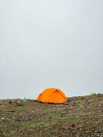 panoramico alpino paesaggio con arancia rinforzata tenda contro il sfondo di un' ghiacciaio su un' alta altitudine altopiano. viaggio concetto. verticale Visualizza. foto