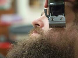 Rifinitura barba con clippers nel un' barbiere negozio. vicino su. foto