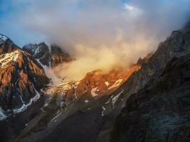 luce del sole nel il montagne. grande ghiacciaio su superiore nel arancia luce. panoramico montagna paesaggio con grande nevoso montagna gamma illuminato di alba sole tra Basso nuvole. foto