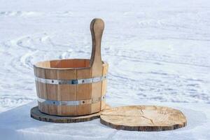 un' di legno vasca per acqua sta su un' fetta di un' albero tronco su ghiaccio su un' sfocato neve sfondo. ferro serraggio anelli Collegare parti di il vasca. orizzontale. foto