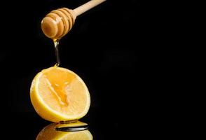 il miele scorre da un cucchiaio a un limone sdraiato su uno sfondo nero con spazio di copia foto