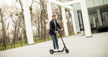 giovane uomo d affari in un abbigliamento casual in sella a uno scooter elettrico da un edificio per uffici in occasione di una riunione di lavoro foto