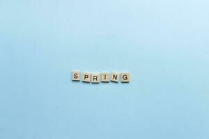 il parola primavera di cui su nel di legno lettere. piatto posare primavera su blu sfondo foto