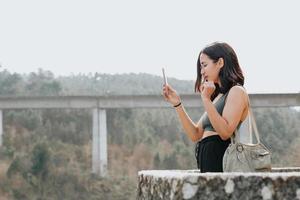 giovane donna in abiti sportivi e occhiali da sole guardando da un balcone con copia spazio durante una giornata di sole controllando il suo telefono e facendo foto