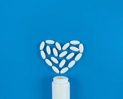 a forma di cuore realizzato con compresse bianche e bottiglia medica su sfondo blu