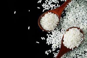 bianca crudo riso nel di legno cucchiai su nero sfondo. crudo cereali di lungo Riso. foto