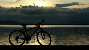 silhouette di un' bicicletta contro il sfondo di il tramonto su il lago foto
