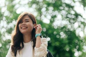 ritratto di un' sorridente giovane asiatico donna ascoltando per musica con auricolari all'aperto foto