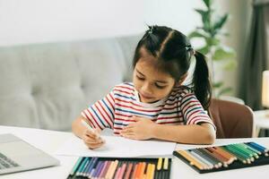 carino asiatico poco ragazza disegno con colore matite a casa foto