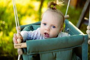 carino poco ragazza nel il oscillazione. bambino swing su il albero nel il giardino. infantile giocando nel il Giardino dietro la casa foto