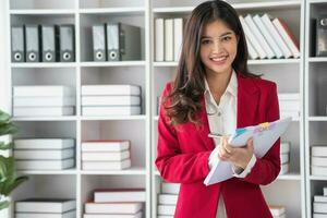 asiatico donna d'affari nel rosso completo da uomo calcolatore azienda i saldi con calcolatrice, computer portatile, e tavoletta su tavolo interno di donna d'affari ufficio a il moderno postazione di lavoro. foto