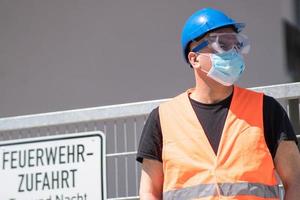 operaio edile che indossa elmetto blu, giubbotto riflettente e maschera chirurgica protettiva foto