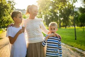 ritratto di contento singolo madre con sua Due figli maschi nel parco su soleggiato giorno. ragazzi siamo mangiare ghiaccio crema. foto